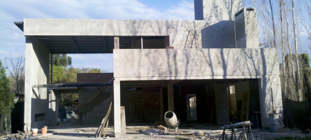 Vivienda de dos plantas en construcción con fachada revocada y hormigonera