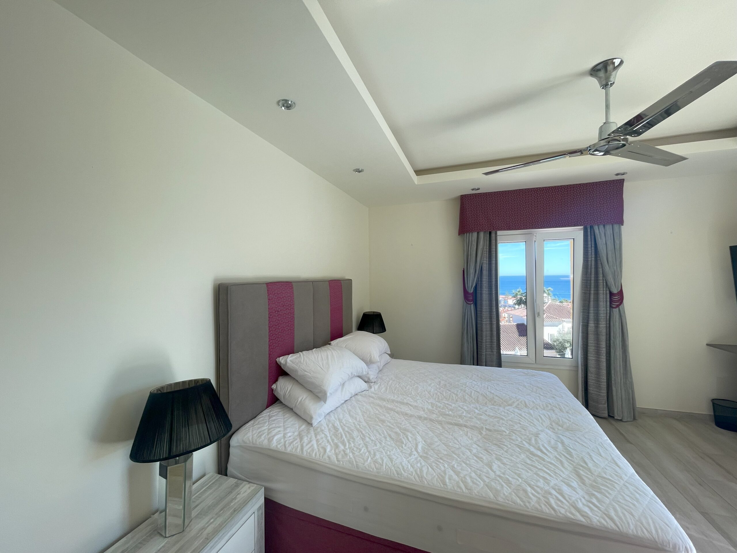 Dormitorio existente con cama doble, ventilador de techo y balcón con vistas al mar