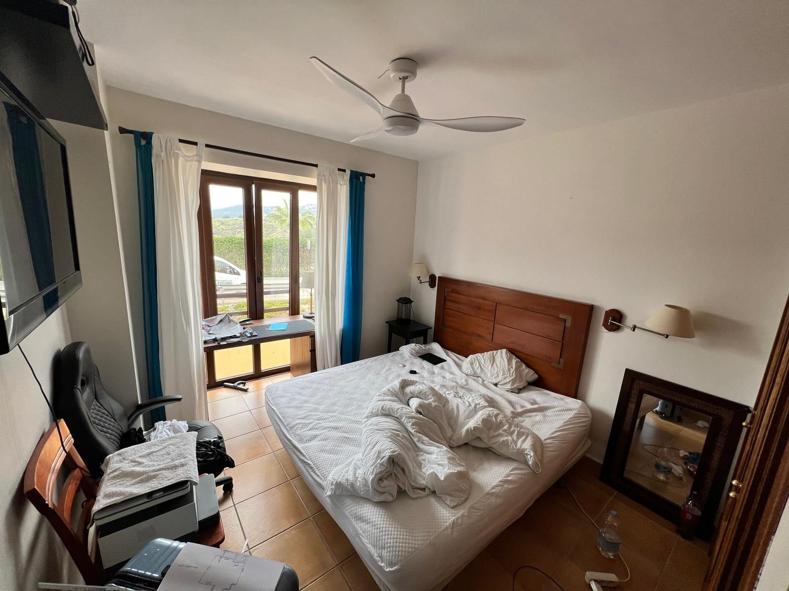 Dormitorio existente con cama de cabecero de madera, silla de oficina y ventilador de techo