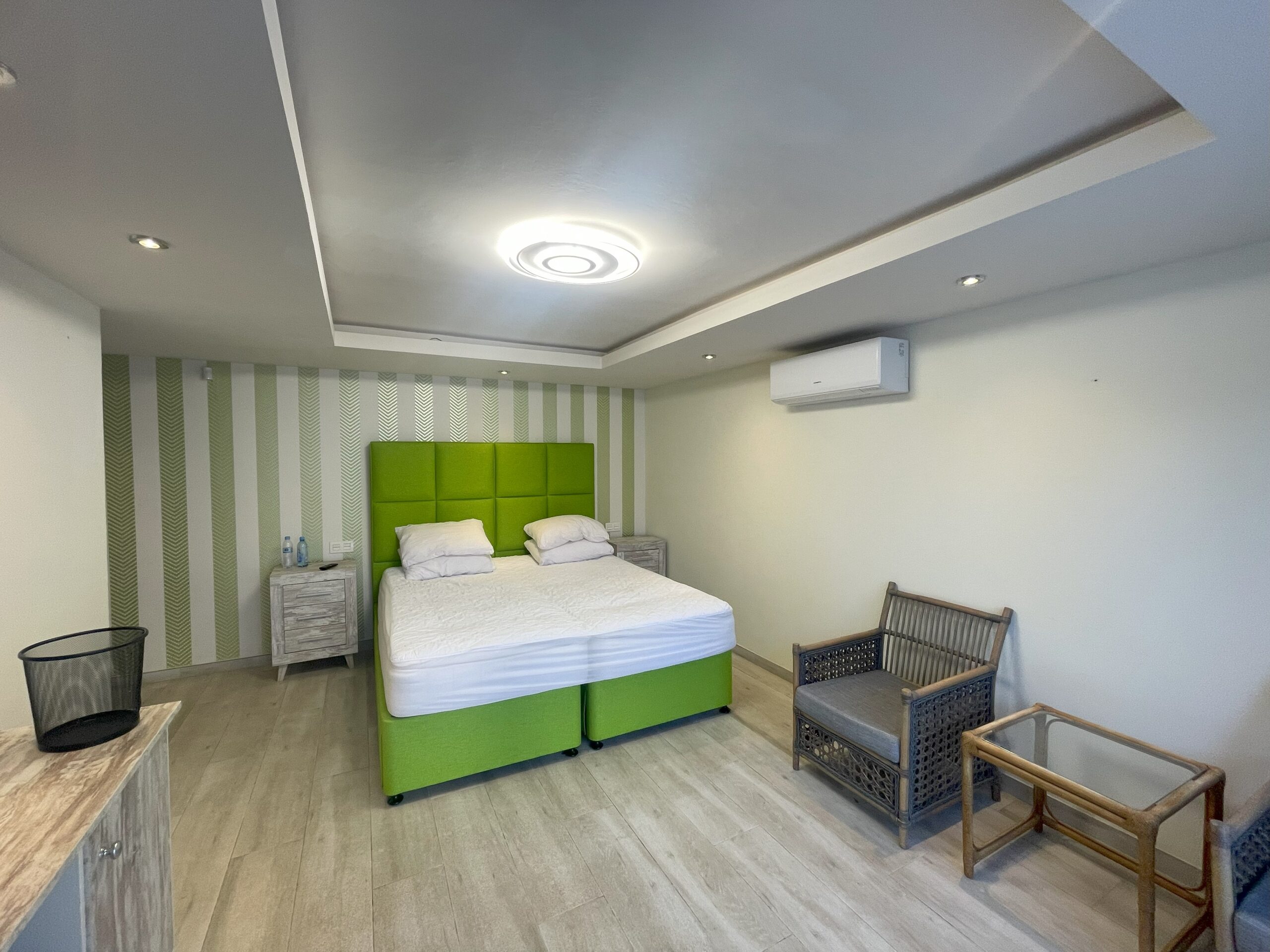 Suite existente con cama doble verde, papel de rayas y sillones de madera