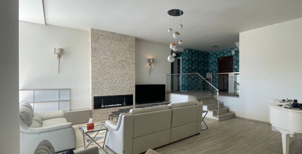 Salón contemporáneo con sofás claros, chimenea revestida de piedra y escalera con barandilla de vidrio