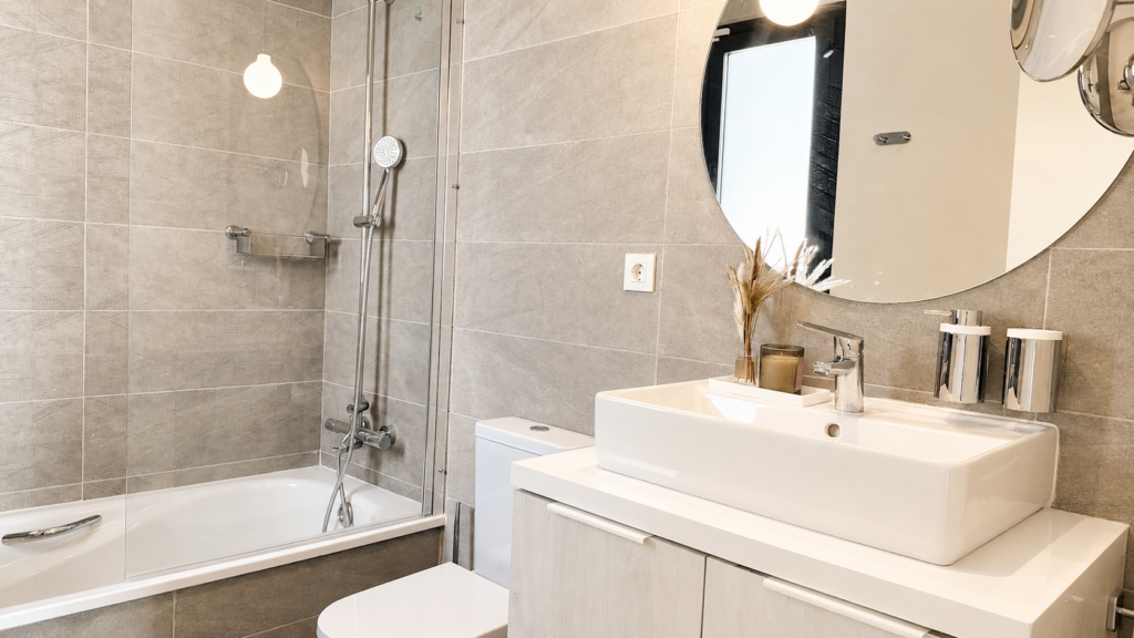 Baño en tonos claros con lavabo sobre encimera y espejo redondo en Manilva